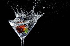 a martini glass with water splashing on it and fruit in the middle, against a black background