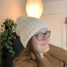 a woman wearing glasses and a knitted hat in front of a plant on the wall