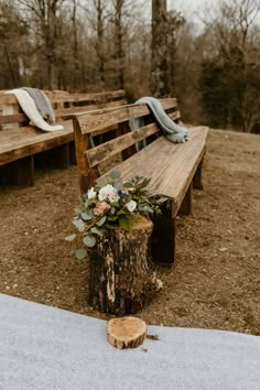 a wooden bench sitting on top of a field next to a tree stump with flowers in it