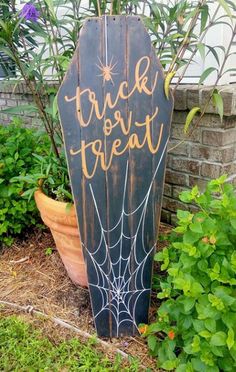 a wooden sign that says trick or treat in front of some flowers and plants with spider webs on it