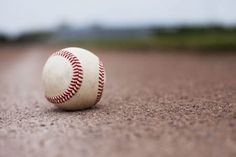 a baseball sitting on top of a field next to a dirt field with grass and trees in the background