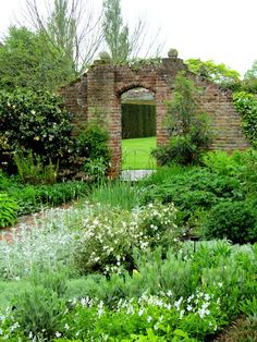 an old brick building surrounded by lush green plants and flowers in the foreground, with a doorway leading into it