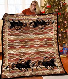 a woman is holding up a quilt with horses on it in front of a christmas tree