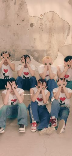 a group of young boys sitting next to each other on the ground with their hands covering their eyes