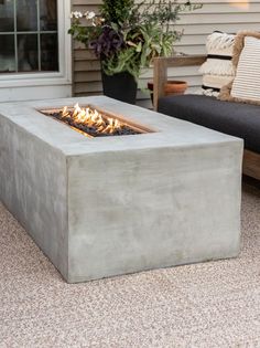 a concrete fire pit sitting on top of a patio next to a couch and potted plant