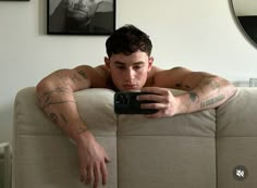 a shirtless man taking a selfie with his cell phone on a couch in the living room