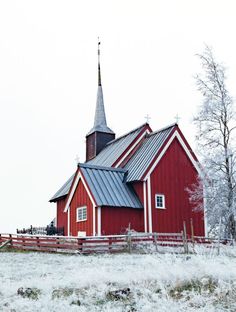 a red barn with a steeple and a fence in the foreground on a snowy day