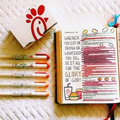 an open bible next to some markers and pencils on a white sheet with red writing