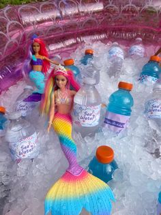 barbie dolls are sitting in an ice bucket filled with water and plastic mermaid tailes