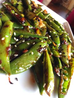 a white plate topped with green beans covered in sesame seeds