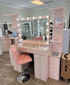 a pink vanity with lights on it and a stool in front of the mirror that is lit up