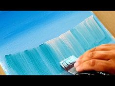 someone using a brush to paint an ocean scene with blue and green colors on the canvas