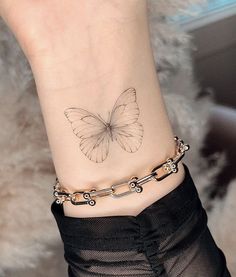 a small butterfly tattoo on the ankle is shown in black and grey colors, with an intricate chain around it