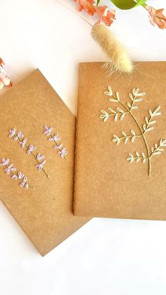 two brown notebooks with embroidered flowers on them