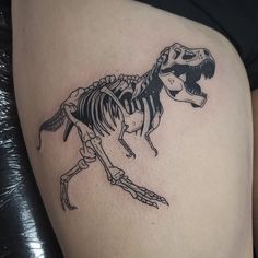 a black and white photo of a dinosaur skeleton tattoo on the side of a woman's thigh