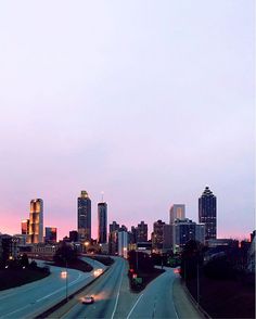 the city skyline is lit up at dusk with cars driving on the road in front of it