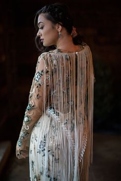 a woman in a white dress with long sleeves and fringes on her back, looking off to the side