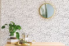 a desk with a mirror, plant and books on it in front of a polka dot wallpaper