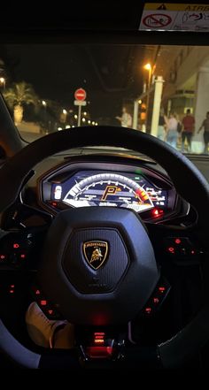 the steering wheel and dashboard of a car at night with people in the street behind it