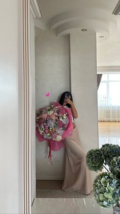 a woman in a long dress holding a bouquet of flowers and taking a selfie