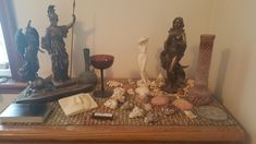 there are many statues on the table with shells and other items around it, including candles