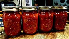 four jars filled with red sauce sitting on top of a wooden table