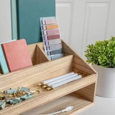 a wooden desk organizer with pens, notebooks and other office supplies in it next to a potted plant