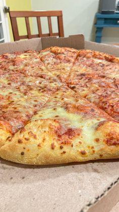 a large cheese pizza sitting on top of a cardboard box next to a wooden table