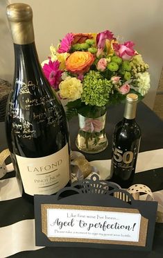 a bottle of wine sitting on top of a table next to a vase filled with flowers