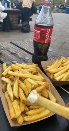 french fries with ketchup and mayonnaise sitting on a picnic table next to a bottle of soda