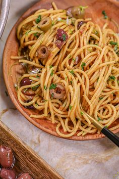 pasta with mushrooms and parsley in a wooden bowl on a marble counter top next to olives