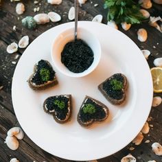 small pieces of bread with black cavia in the middle on a white plate next to lemon wedges