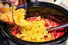 someone pouring sauce into a crock pot filled with pasta and other ingredients to make the dish