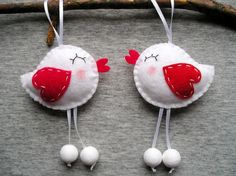 two white birds with red beaks hanging from a branch on a gray surface next to some balls