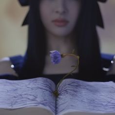 a woman is holding an open book with a flower in her hand and looking at it