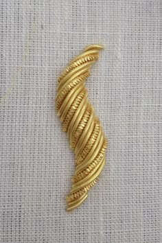 a gold plated metal object on a white fabric background with some thread in the middle