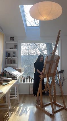 a woman standing next to an easel in front of a window