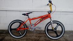 an orange bike parked next to a white brick wall with a yellow and black handlebar