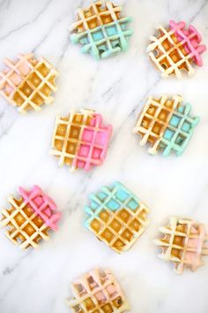 four waffles with different colored toppings on a marble countertop next to each other