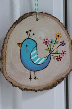 a blue bird hanging on a wood slice with flowers in it's beaks