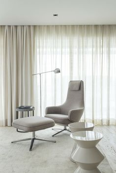 a chair and ottoman in front of a large window with sheer drapes on the windowsill