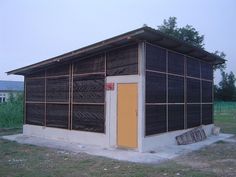 a small building with a yellow door and window on the outside, in an open field