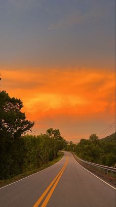 the sun is setting on an empty road with trees and bushes in the foreground