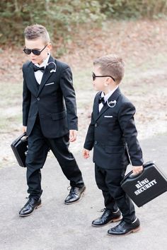 two young boys dressed up in suits and holding briefcases, walking down the street