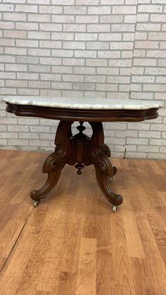 an antique table with marble top on wooden flooring in front of a brick wall