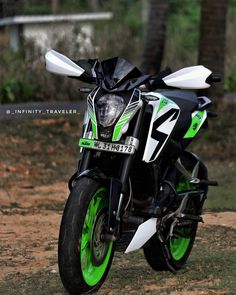 a green and white motorcycle parked on top of a dirt field next to trees in the background