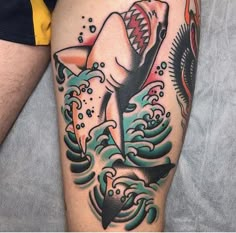 a man's leg with a shark and wave tattoo on the side of his thigh