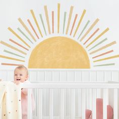 a baby in a crib with the sun painted on the wall behind it,