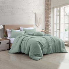 a large bed in a room with white walls and wooden flooring, along with a green comforter