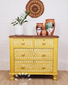 a yellow dresser with two vases on top of it and a plant in the corner